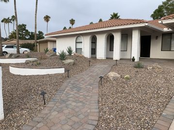 Single-story house with a tiled roof, arched entryway, and xeriscaped front yard featuring rocks, succulents, and a curved brick walkway.
